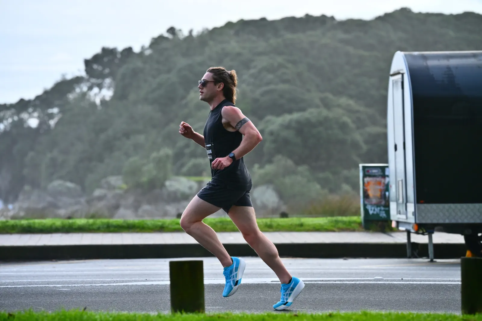 Eli running a road race along the coast in a black singlet and bright blue shoes
